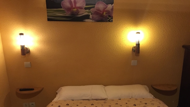 Una habitación de hotel con cama, dos mesitas de noche y luces fijadas a la pared.