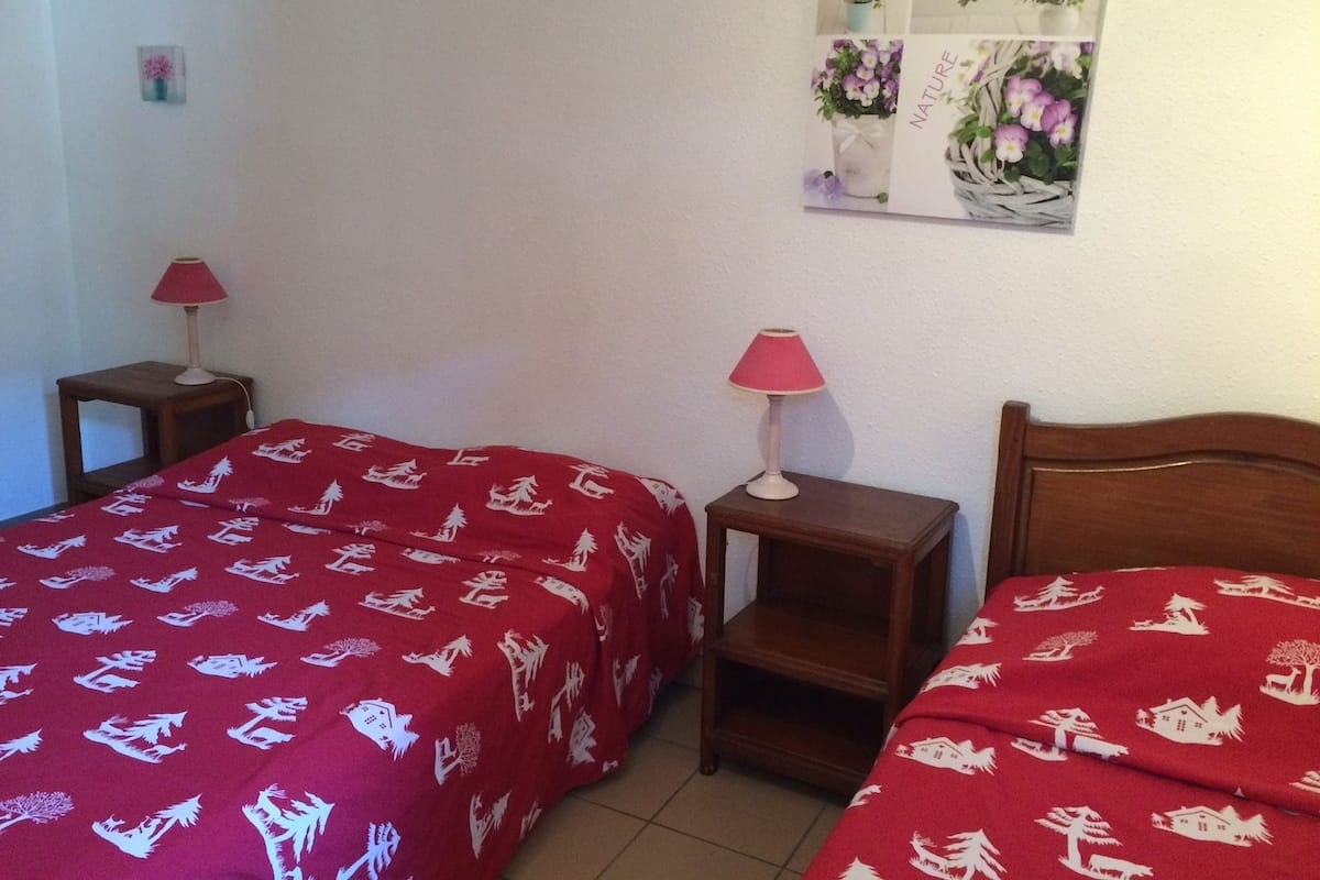 Habitació d'hotel amb dos llits, cadascun amb un llençol vermell que té dibuixos blancs. Hi ha dues taules de nit amb làmpades, i un quadre penjat a la paret que mostra flors i la paraula "NATURE".