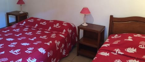 A hotel room with two beds, each with a red bedspread featuring white patterns. There are two bedside tables with lamps, and a wall-mounted picture frame displaying flowers and the word "NATURE".
