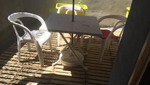 Un pequeño patio con una mesa y sillas, una maceta amarilla y un muro de hormigón.