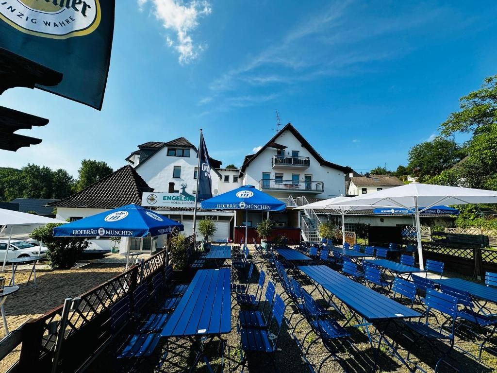 An outdoor seating area with tables and umbrellas, a building with a sign, and a clear sky.
