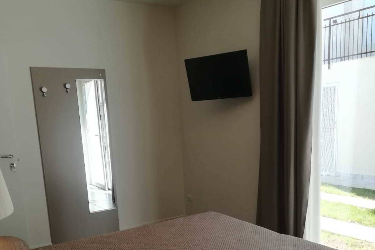 Un dormitorio con cama, puerta, televisión y ventana con cortinas.