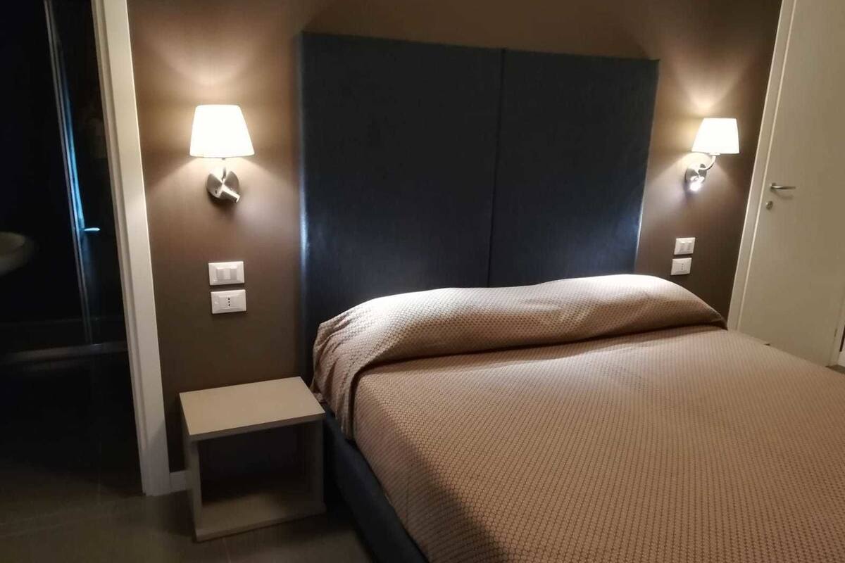 Una habitación de hotel con una cama, lámparas de noche, una mesita de noche y una pequeña mesa.