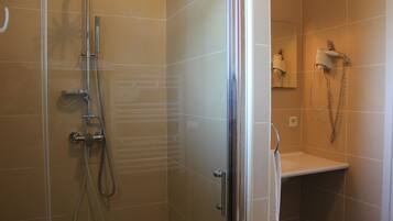 Une salle de bain dotée d’une douche à paroi de verre, d’un porte-serviettes et d’un sèche-cheveux fixé au mur.