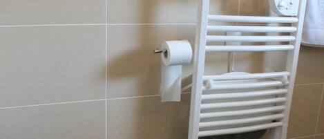 Un baño con inodoro, toallero y un rollo de papel higiénico.