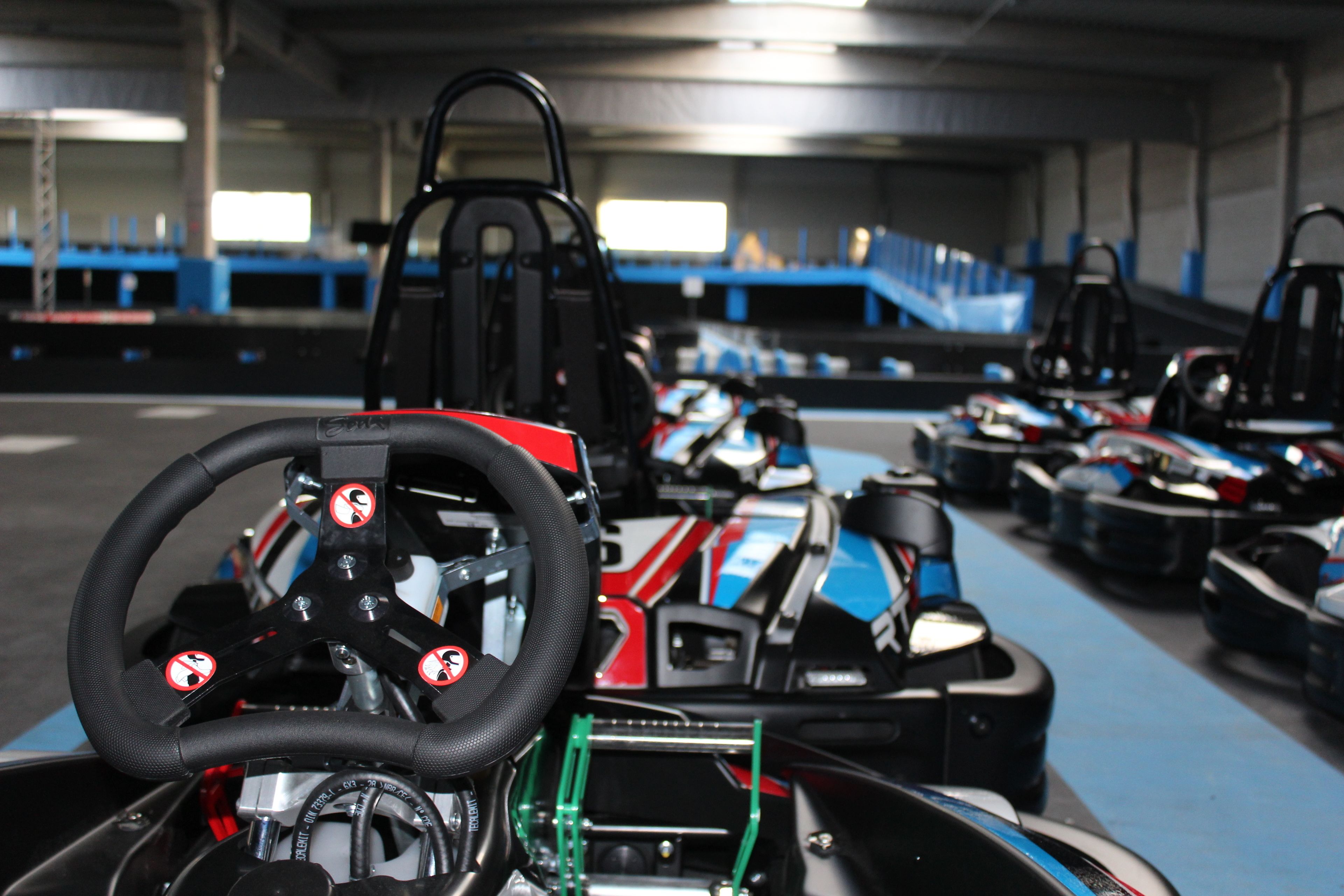 Una pista de karts con varios karts alineados, un volante y un asiento de carreras.