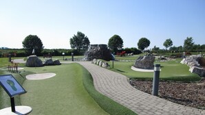 Un campo de golf con un sendero pavimentado, césped verde y diversos elementos de jardinería.