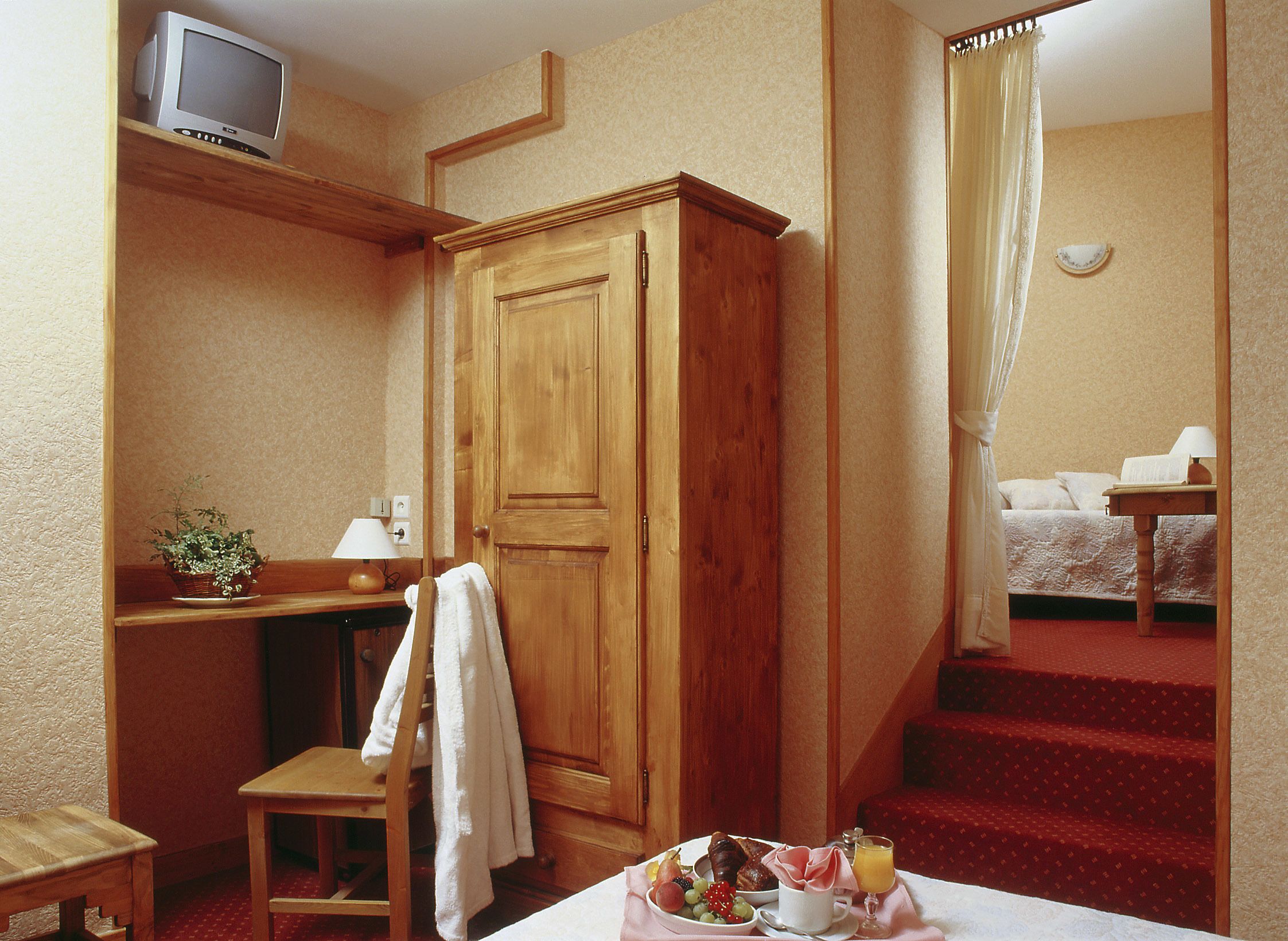 Una habitación de hotel con un armario de madera, un escritorio con televisor, una cama y una escalera con alfombra roja, además de una bandeja de desayuno sobre la mesa.