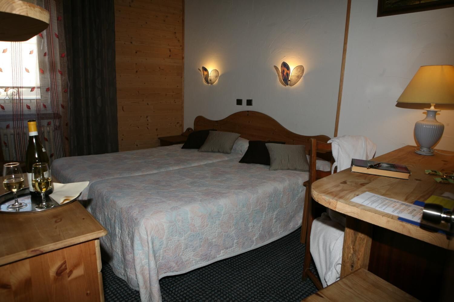 Un lit double avec une tête de lit en bois, deux appliques murales, une table de chevet avec une lampe et une fenêtre avec des rideaux.