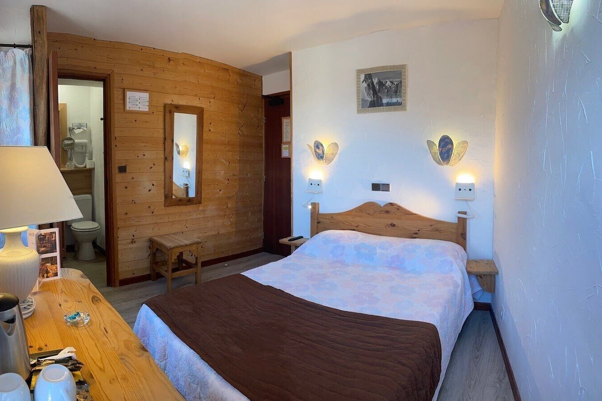 Een kamer met houten lambrisering, een bed, een bureau met lamp, een spiegel en een klein tafeltje.