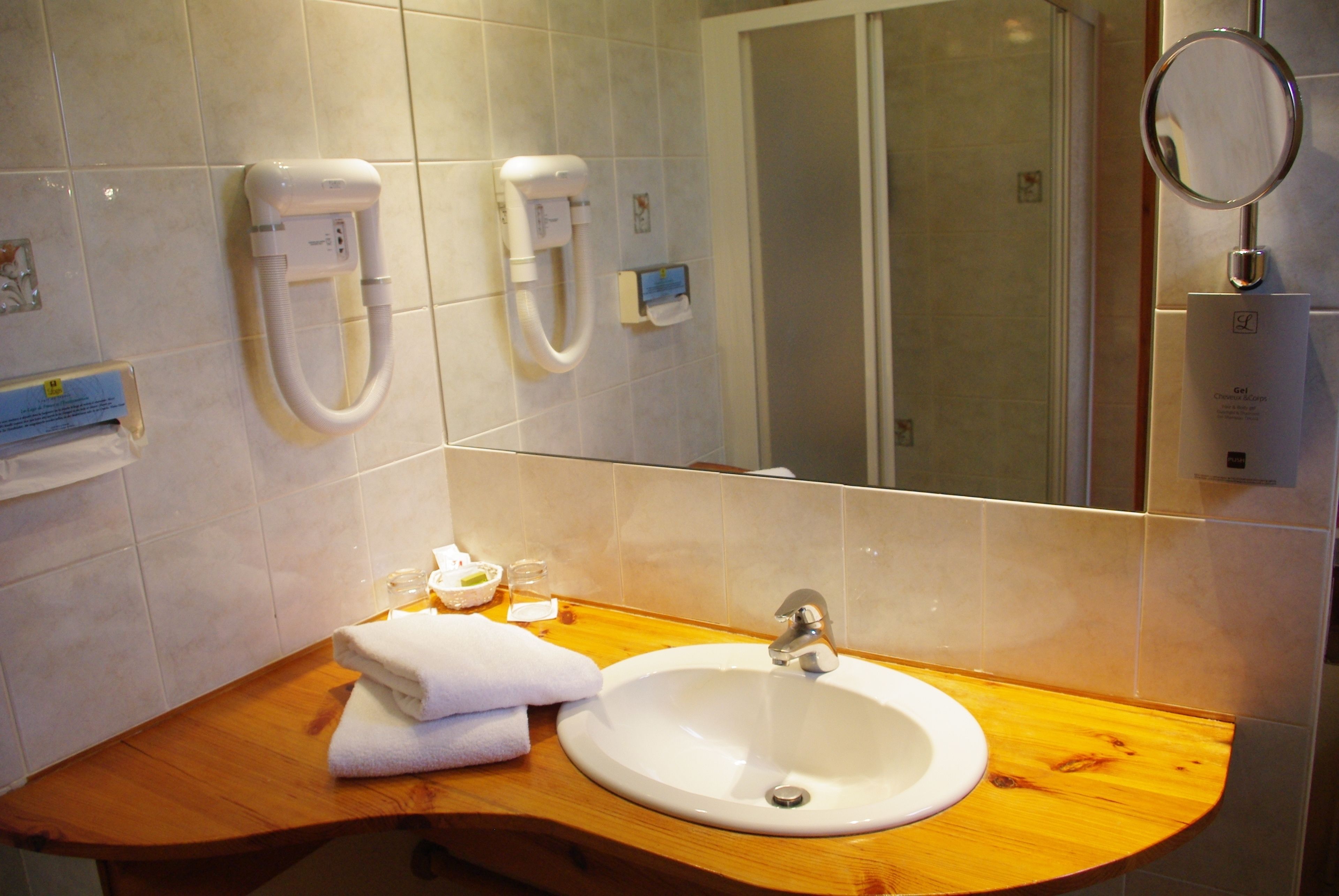 A bathroom with a wooden vanity, a white sink, and two hand dryers mounted on the wall.