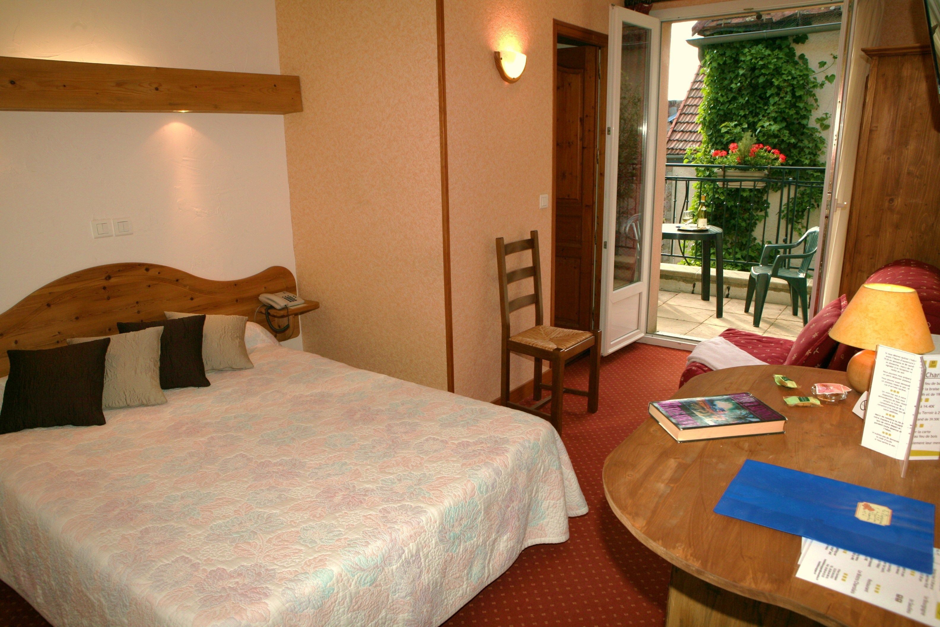 A hotel room with a bed, a wooden headboard, a chair, a table with a lamp, and a view of the outside balcony.