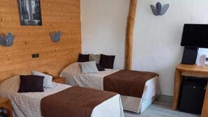Una habitación de hotel con dos camas, paredes de madera, una mesita con una lámpara y un cuadro en la pared.