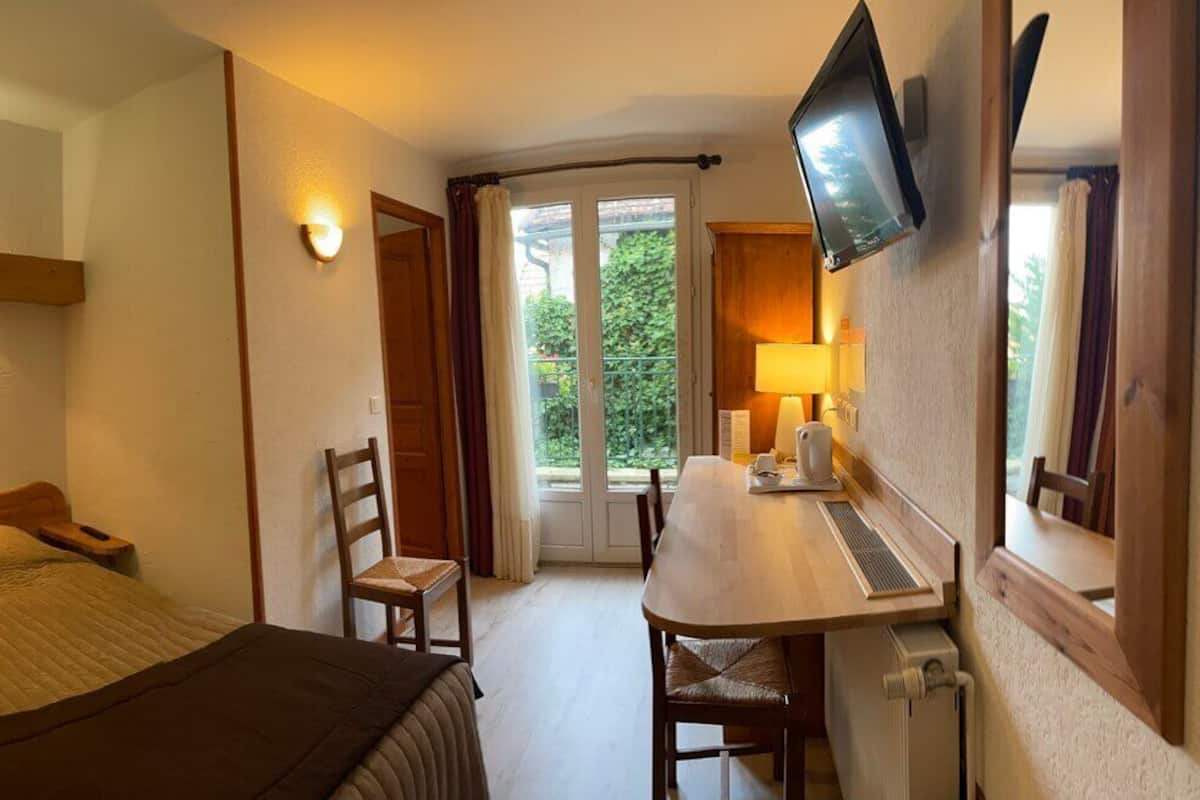 Hotelkamer met een bed, bureau, stoel, televisie en raam met gordijnen.