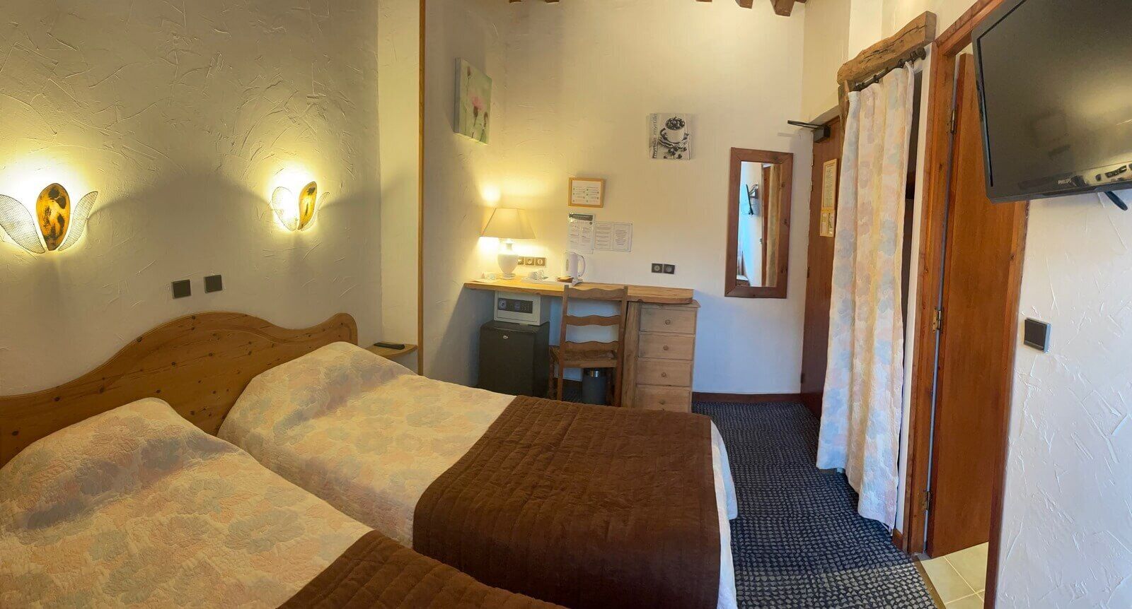 Une chambre d’hôtel avec deux lits, un bureau avec une lampe, une télévision et une salle de bain avec un rideau de douche.