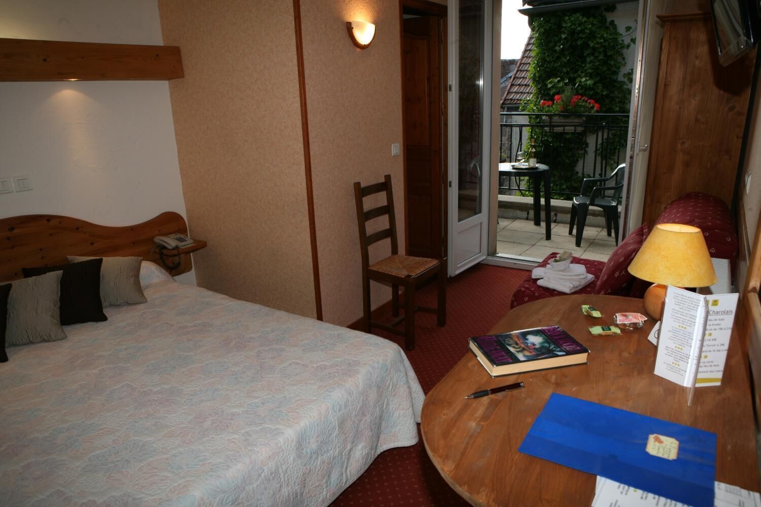 Ett hotellrum med en säng, en stol, ett bord med en lampa, en bok och en meny.