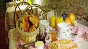 Desayuno con pan, bollería, fruta y bebidas sobre una mesa.