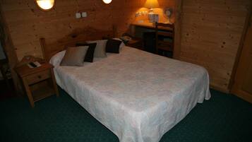 Een houten kamer met een bed, nachtkastje, lamp en wandlampen.