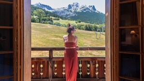 A woman standing on a balcony with a view of a mountain range. - Montana Chalet Hôtel Spa (Enchastrayes)