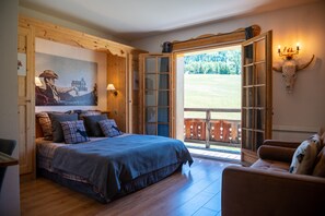 Un dormitorio con una cama grande, cabecera de madera, un cuadro de un vaquero, una puerta de madera y vistas a un patio cercado.