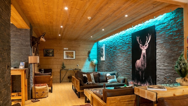 A cozy cabin interior with a stone wall, wooden furniture, and a deer painting. - Montana Chalet Hôtel Spa (Enchastrayes)