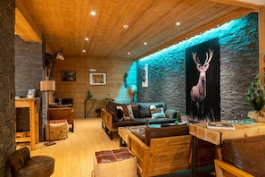 Un interior de cabaña acogedor, con pared de piedra, muebles de madera y un cuadro de un ciervo.