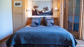 A bed with a blue blanket and plaid pillows, a wooden door, and a painting of a cowboy on the wall.