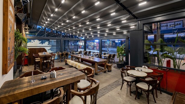 A restaurant with wooden tables and chairs, a high ceiling with lights, and large windows offering views of the street. - HAY Hotel Alsancak (Izmir)