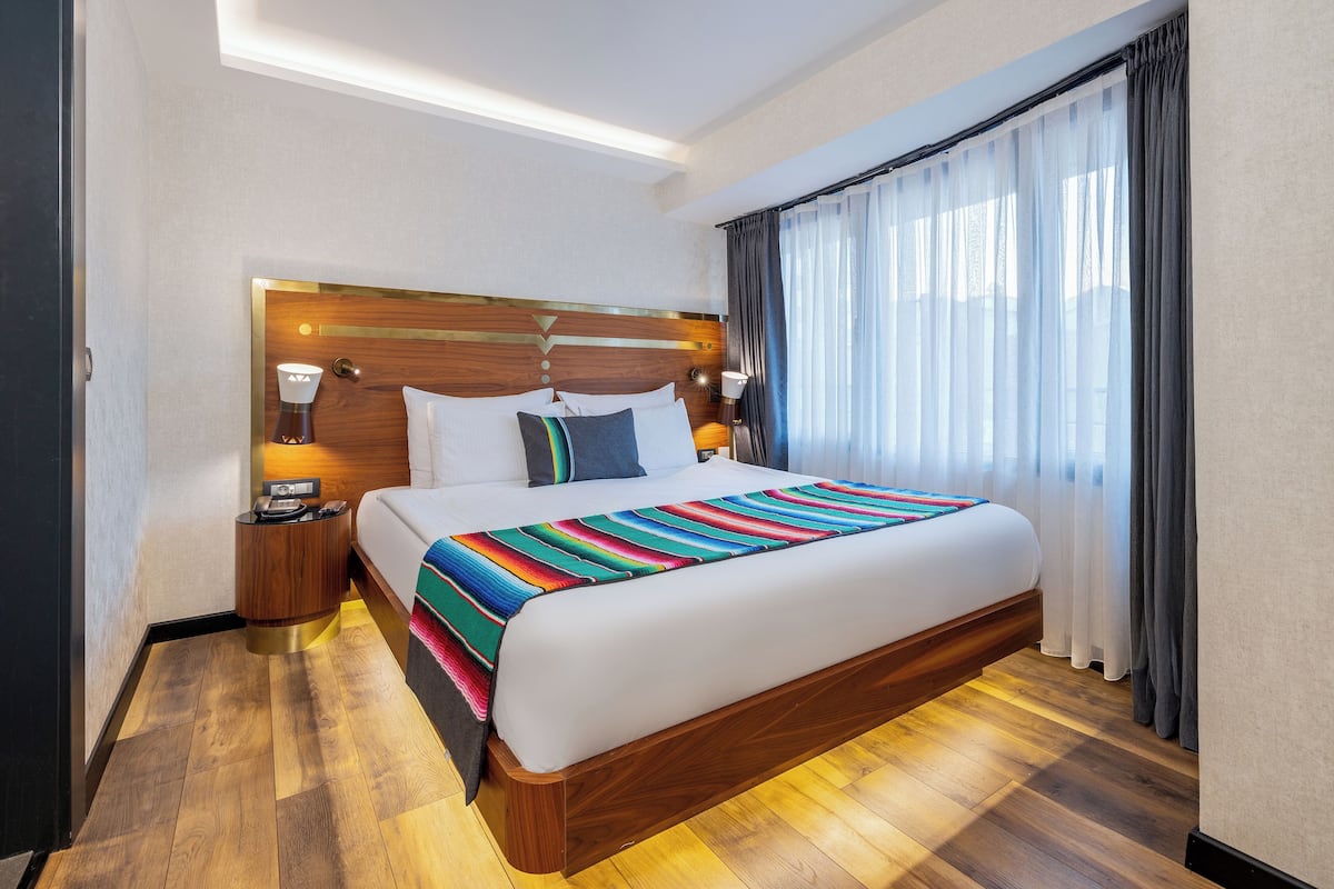 A hotel room with a wooden bed, a nightstand, a lamp, and a window with curtains.