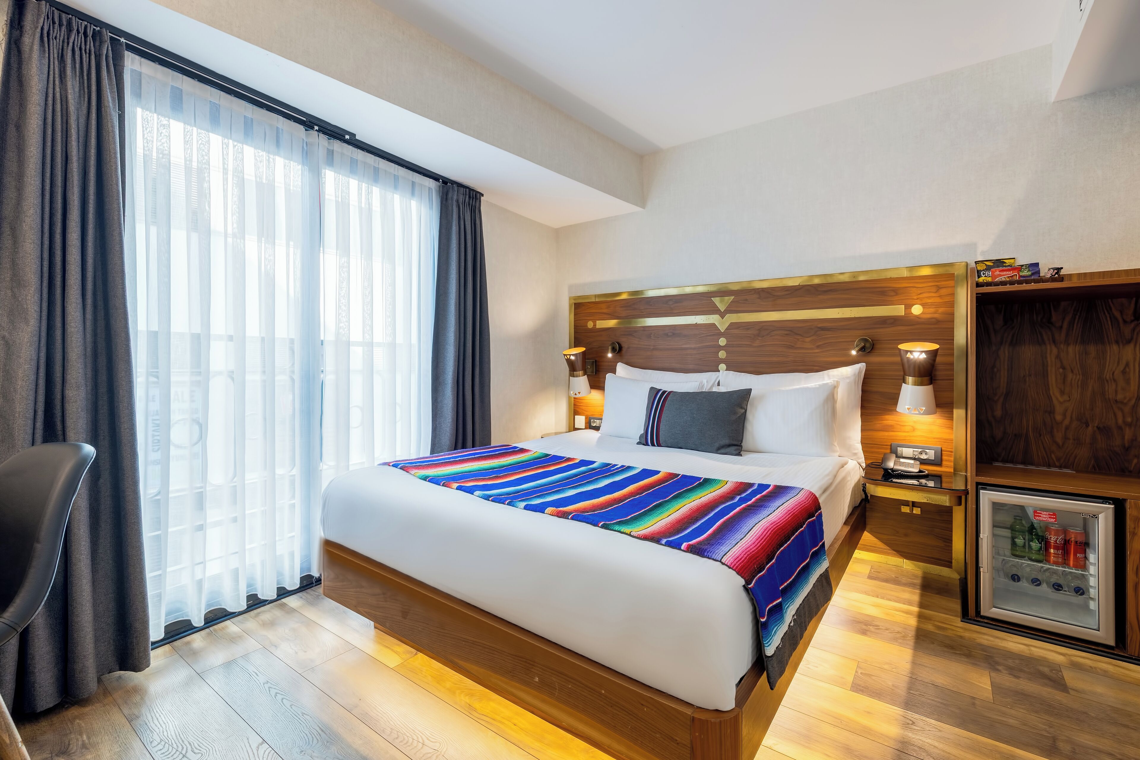 Habitación de hotel con una cama grande, una mesita de noche con lámpara, un refrigerador pequeño y una silla.