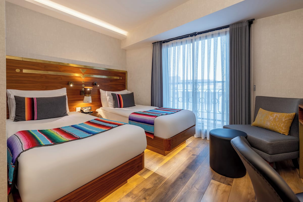 A hotel room with two beds, a sofa, a small table, and a view of the city.