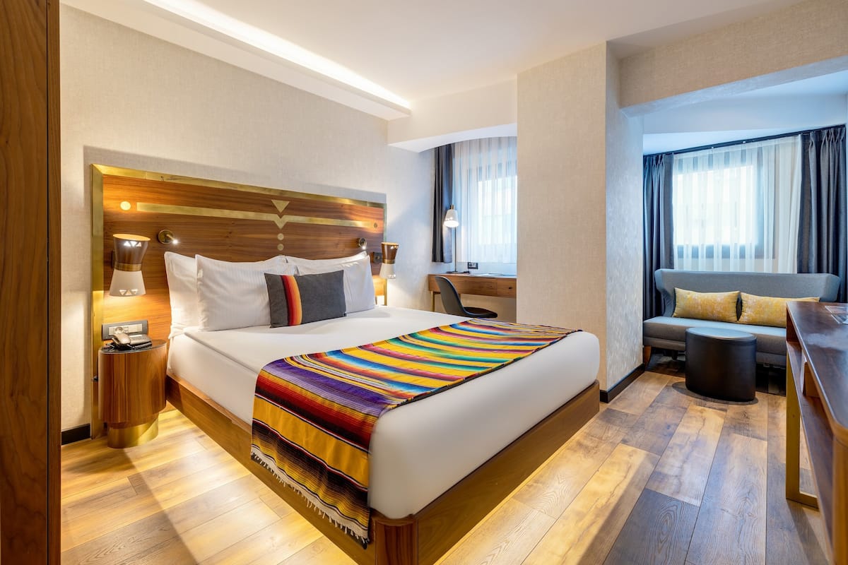 A hotel room with a large bed, a desk, a chair, and a sofa.