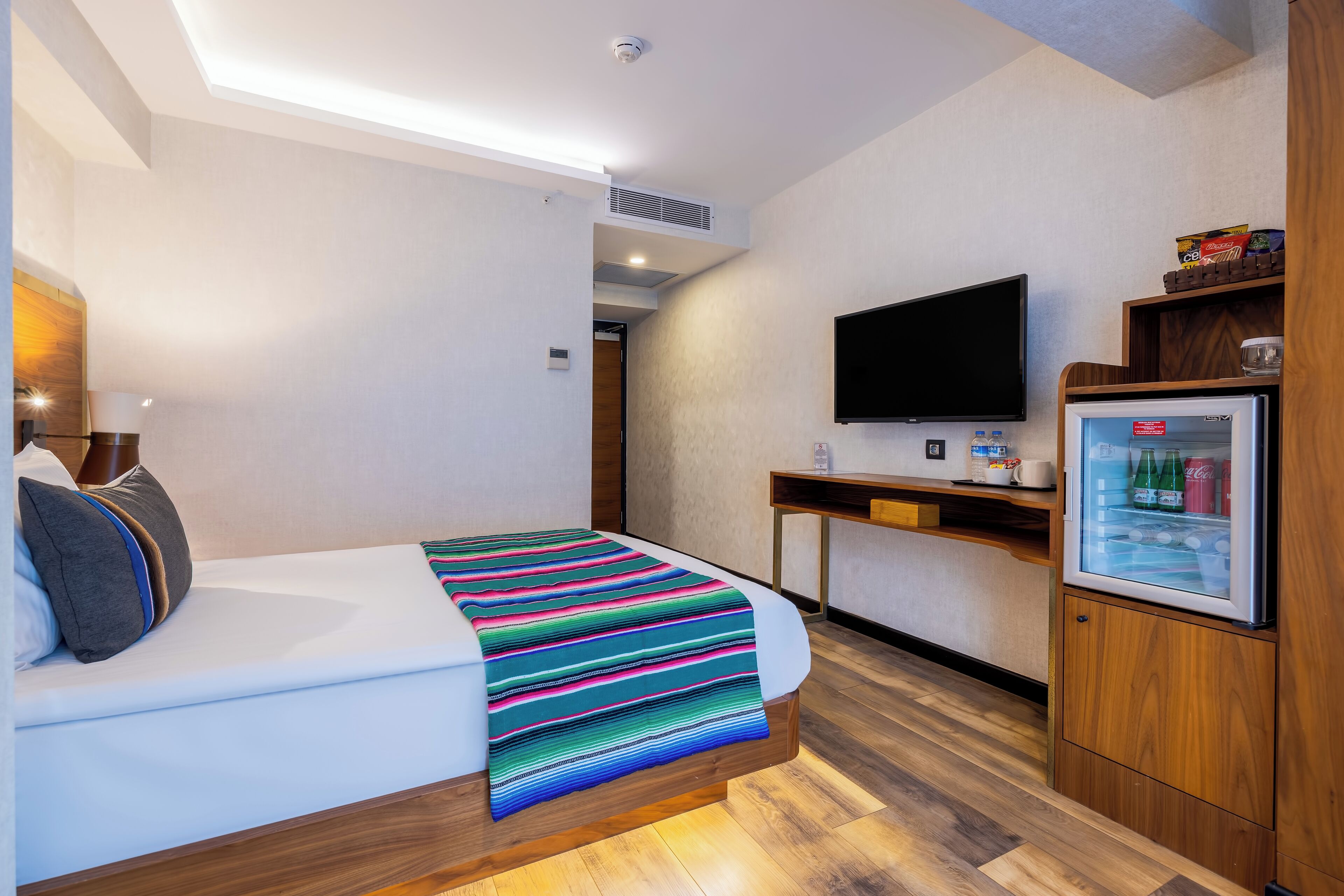Habitació d'hotel amb llit, televisió, nevera petita i escriptori.