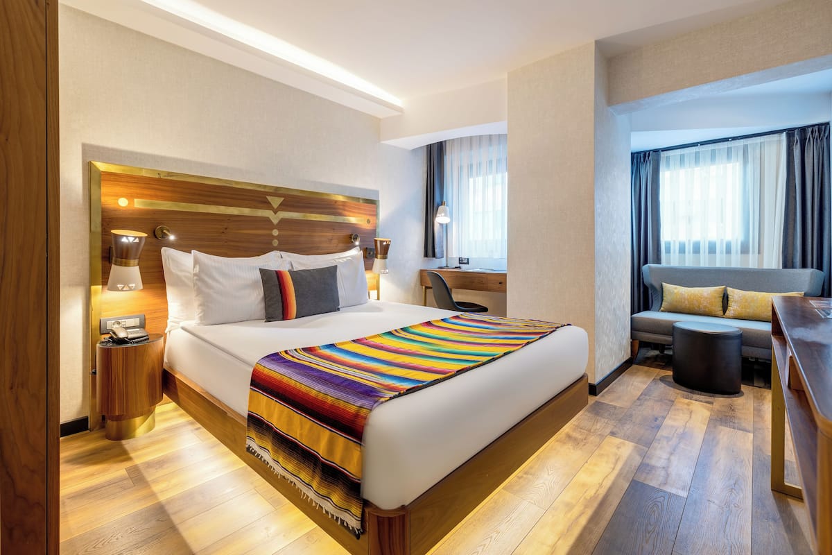 A hotel room with a large bed, bedside tables, a desk, and a sofa.