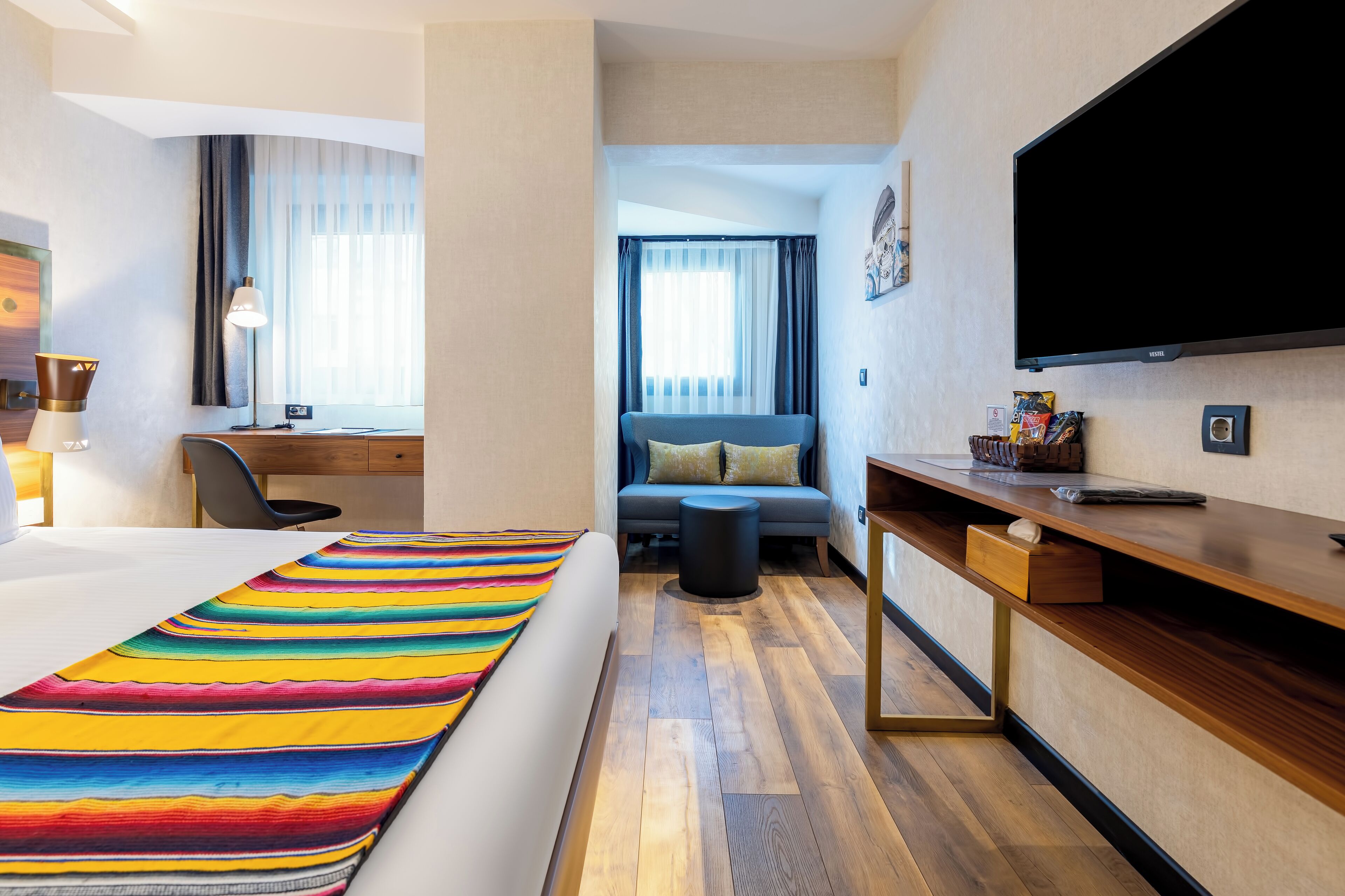 Ein Hotelzimmer mit Bett, Schreibtisch, Fernseher und einer Sitzecke mit einer Couch und einem kleinen Tisch.