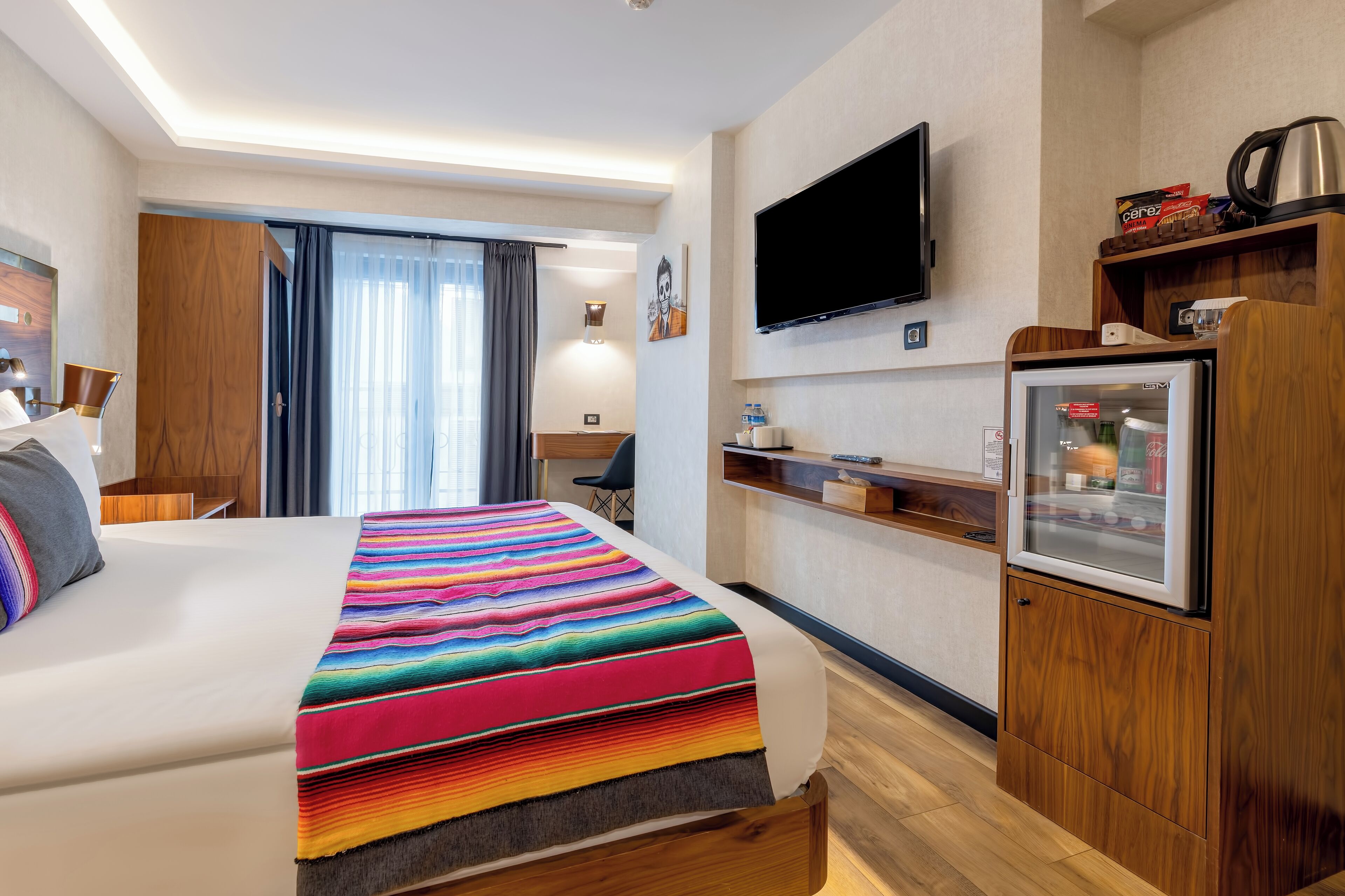 A hotel room with a large bed, a television mounted on the wall, a refrigerator, and a wooden cabinet.