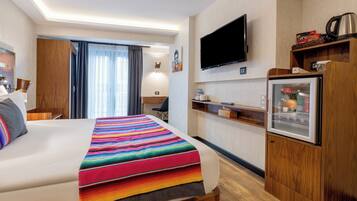 A hotel room with a large bed, a television mounted on the wall, a refrigerator, and a wooden cabinet.