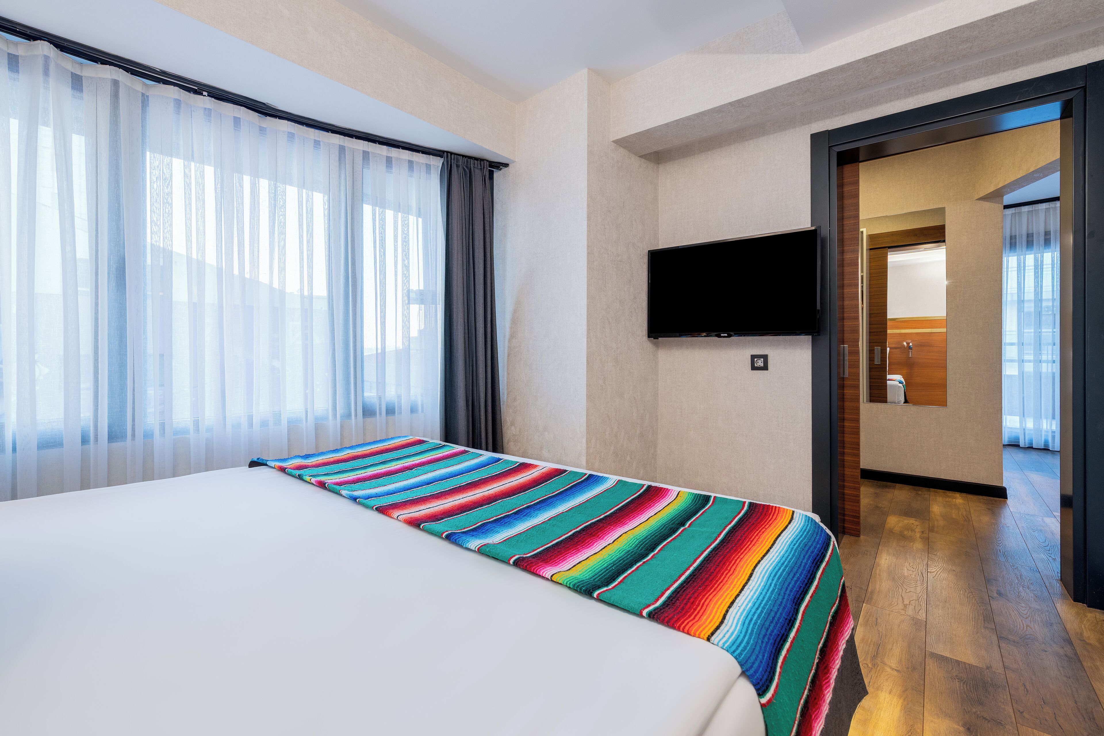 A hotel room with a bed, a TV mounted on the wall, and a view of the hallway.