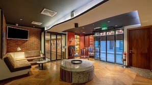 A lobby with a brick wall, a round marble table, leather sofas, and a fire extinguisher near the exit. - HAY Hotel Alsancak (Izmir)