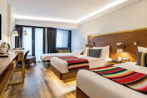 A hotel room with two beds, a desk, a chair, and a large window with curtains.