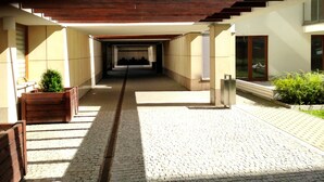 Un pasillo exterior cubierto con suelo de ladrillo, bancos de madera y plantas en macetas.