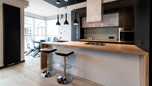 Una cocina moderna con encimera de madera, lámparas colgantes negras y electrodomésticos de acero inoxidable.