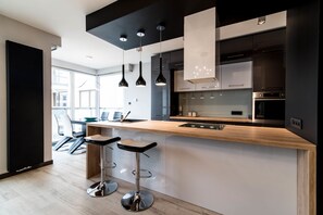 A modern kitchen with a wooden countertop, black pendant lights, and stainless steel appliances. - Ericius Apartments - Ericius Group (Poznan)