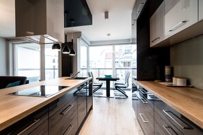 Una cocina moderna con una isla central, armarios negros y vistas a la ciudad a través de amplios ventanales.