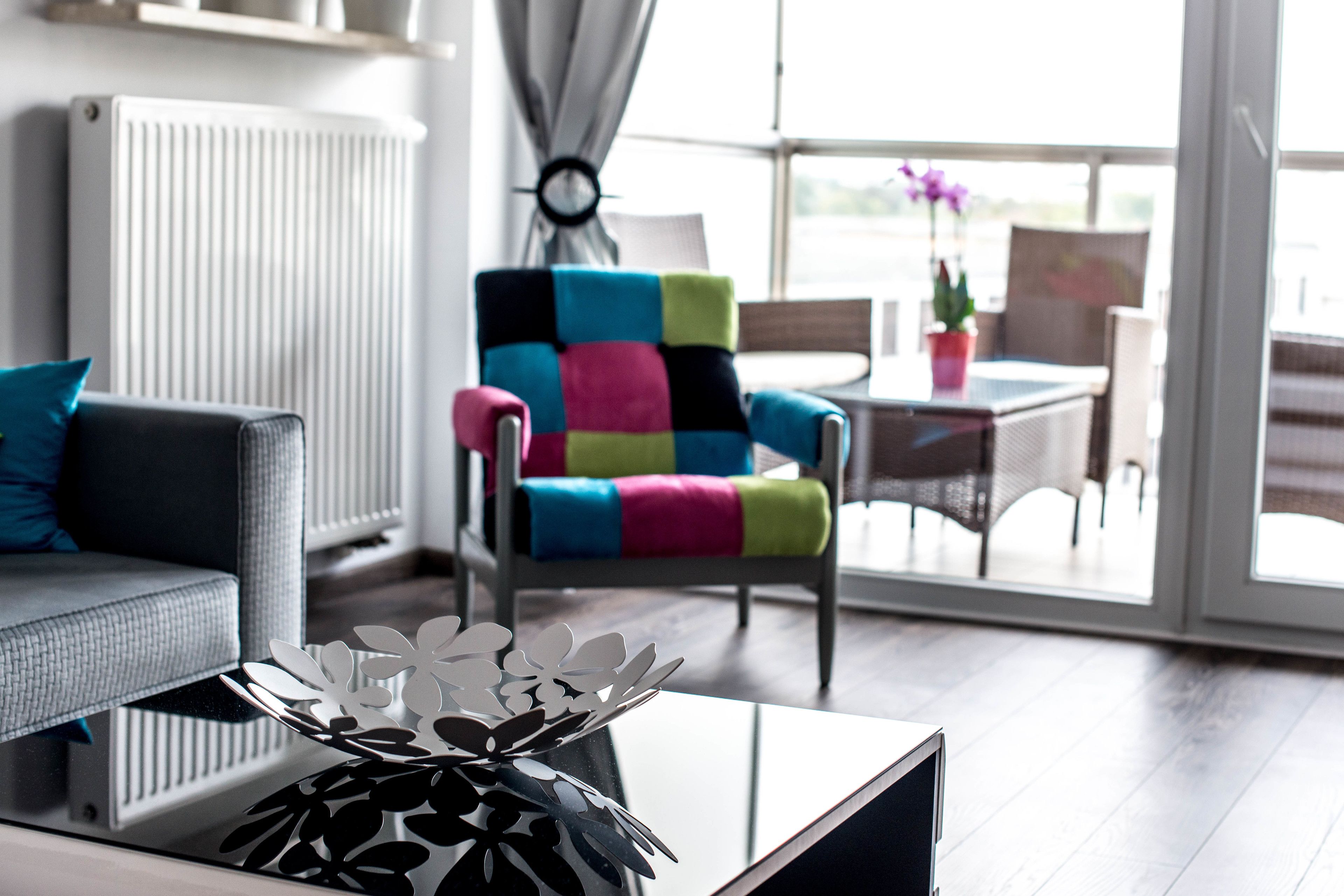 A modern living room with a colorful armchair, a sofa, and a glass coffee table.