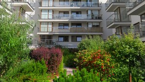 Un edificio residencial de varios pisos con balcones, rodeado de abundante vegetación y plantas con flores.