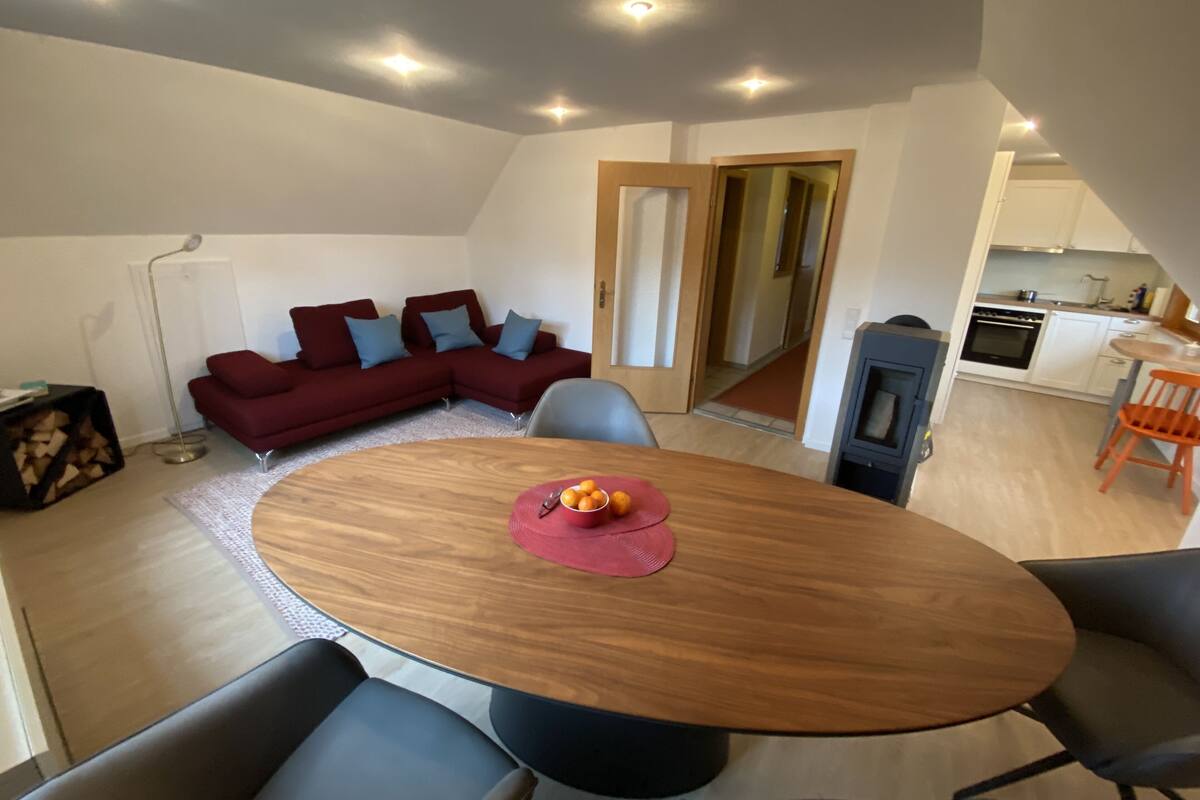 Un espace de vie moderne comprenant un coin repas, un canapé d’angle rouge, une cuisine et un escalier apparent.