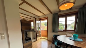 A modern kitchen with a built-in oven and a dining area with a round table and teal chairs. - Pia's Nature Retreat (Neukirch)