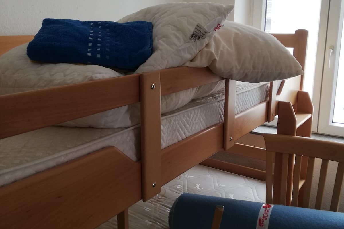 A bunk bed with a blue blanket and a pillow, a wooden chair, and a window with blinds.