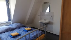 A small, narrow room with a bed, a bedside table, a sink, and a mirror. - Gästehaus Heigeleshof (Ulm)